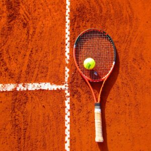 Tennis racket and ball on red clay court, ideal for sports-themed content.
